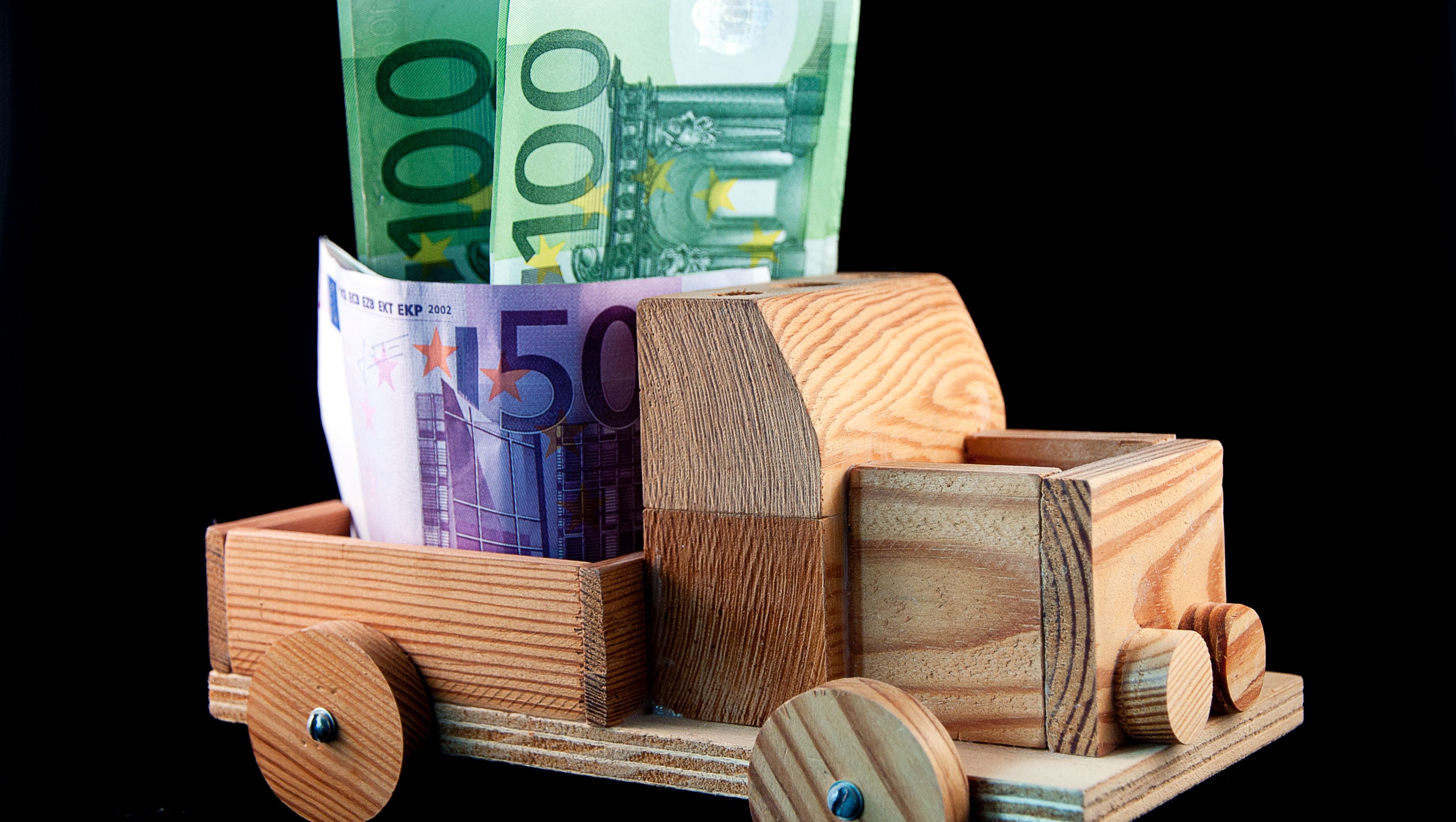 Spielfahrzeug aus Holz mit Euroscheine im Kofferraum